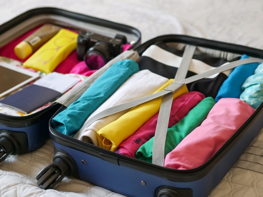 Troler de cabină deschis pe pat, cu haine rulate și cuburi de organizare pregătite pentru o vacanță